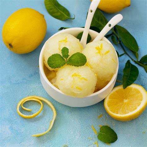 Fotografija elegantnega kozarca za penino, v katerem je limonin sorbet s penino, okrašen z rezino limone in meto.