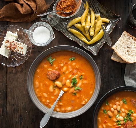 Flat lay of all the fresh ingredients for pasulj: beans, smoked meat, onion, garlic, carrots, paprika, tomatoes, bay leaf