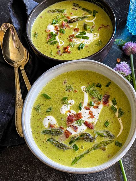A bowl of creamy asparagus soup garnished with asparagus tips and herbs.