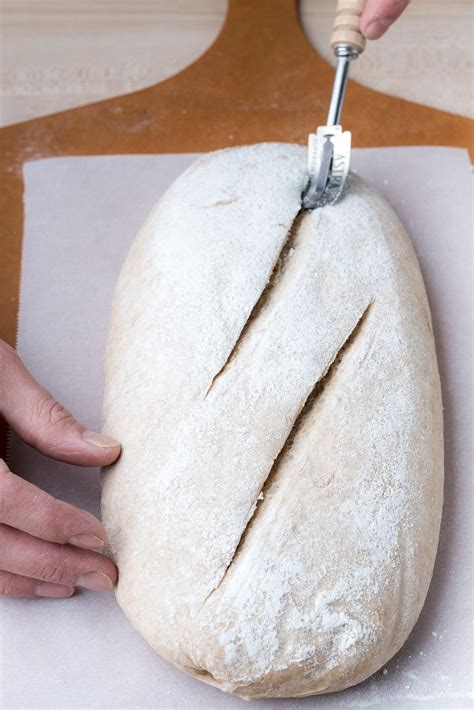 Photo of a sourdough loaf being scored with a lame before baking