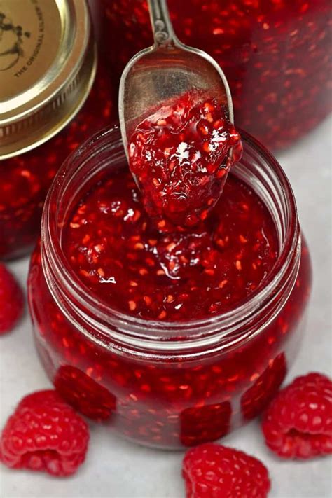 Thematic photo of a jar of smooth raspberry jam without seeds next to fresh raspberries and pancakes.