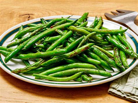 Thematic photo of fresh green beans on a wooden table, possibly with some pork meat in the background