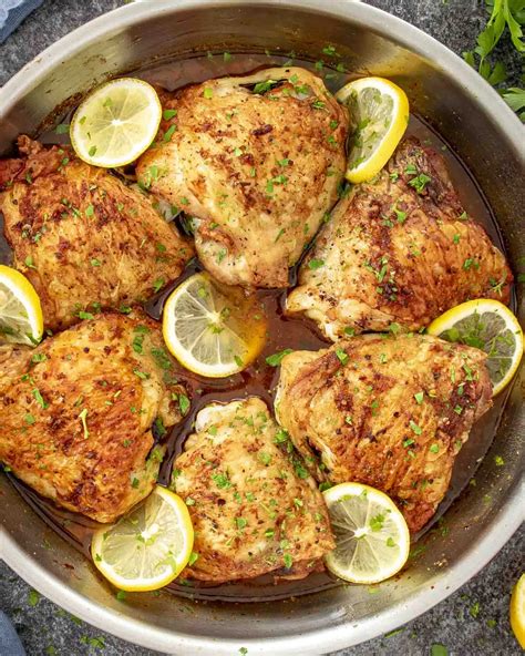 Close-up of golden brown chicken thighs with lemon slices and fresh thyme, roasted in a pan with caramelized onions.