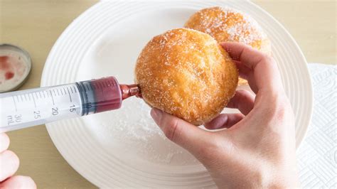 Thematic photo of a pastry chef filling a donut with jam using a syringe
