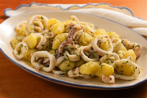 Thematic photo of potato salad with squid in a bowl, garnished with lemon and parsley