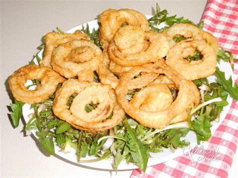 Prikaz pripravljenih, zlato-rjavo ocvrte čebulnih obročkov, postreženih s solato in omako.