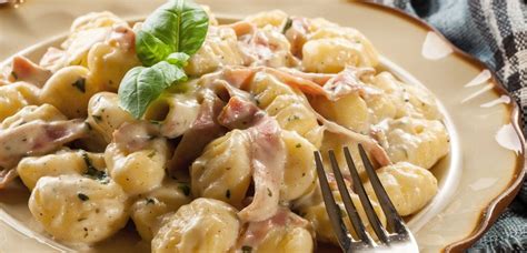 Njoki s šampinjoni in pršutom na krožniku, posuti s peteršiljem in parmezanom