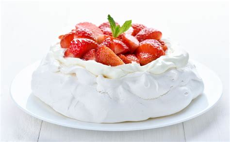 fotografija elegantne torte Pavlova, okrašene s svežimi jagodami in smetano na krožniku