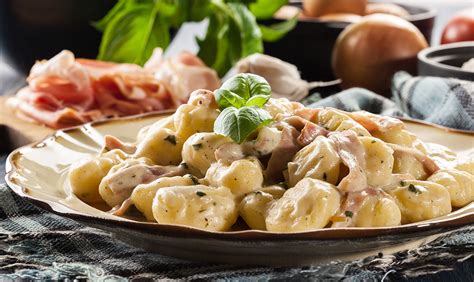 Tematska fotografija tortelinov s pršutom in smetanovo omako na krožniku, posuti s peteršiljem in parmezanom