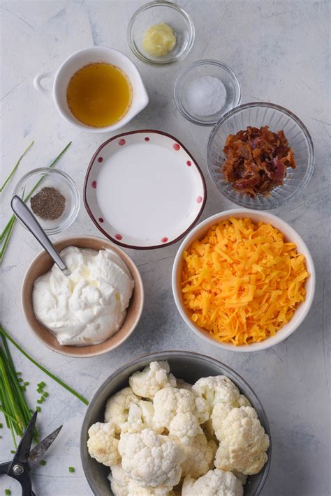 Ingredients for gratiniran cvetačni narastek, including cauliflower florets, sour cream, eggs, cheese, and spices.