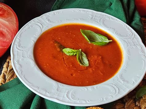 Pripravljena, gladka paradižnikova juha v skledi, okrašena s svežimi zelišči