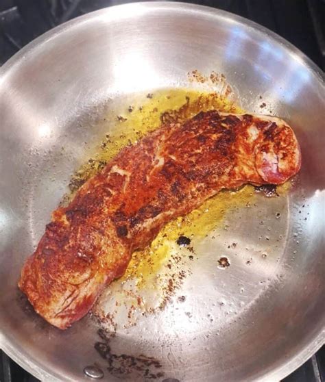 Photo of pork tenderloin searing in a pan before going into the oven