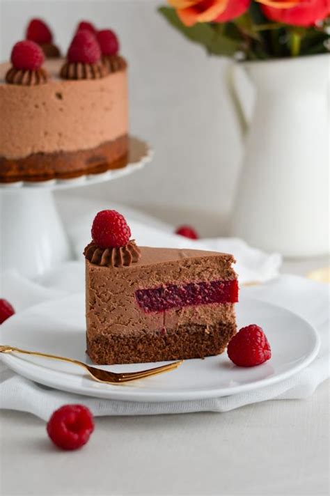 Fotografija elegantne čokoladne torte, okrašene z malinami in meto.