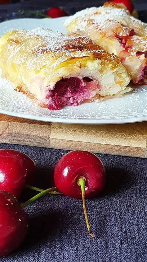 fotografija sveže pečenega zavitka s češnjami in skuto, posutega s sladkorjem v prahu