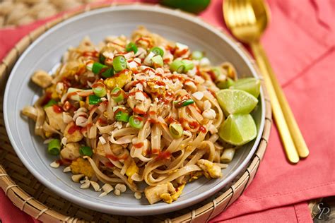 Pripravljen Pad Thai s piščancem na krožniku, okrašen z arašidi in zelišči
