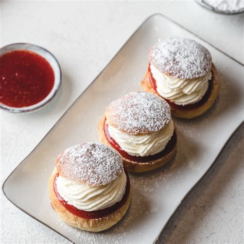 Fotografija zlato-rumenih, okroglih krofov s sladkorjem v prahu, ki so polnjeni z marmelado.