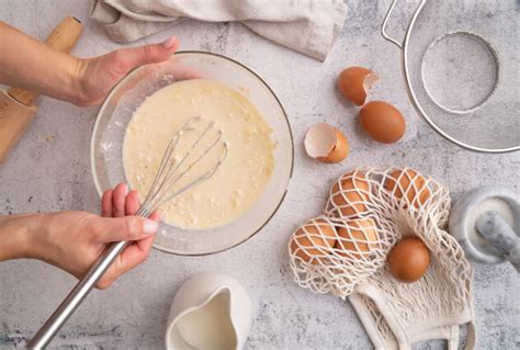 Pripravljen kolaž fotografij, ki prikazujejo posamezne faze priprave torta: stepanje jajc, mešanje sestavin, pečenje biskvita, priprava kreme, dodajanje jagodnega preliva in končni izdelek.