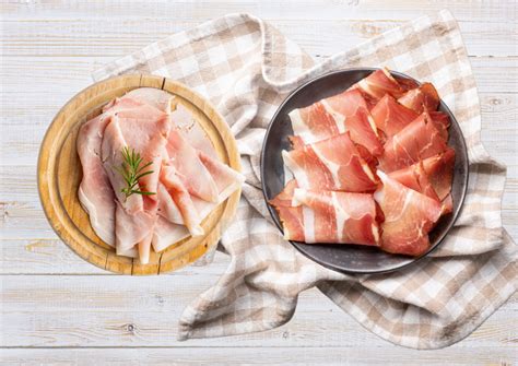 različne vrste italijanske šunke (prosciutto cotto, prosciutto crudo) na leseni deski