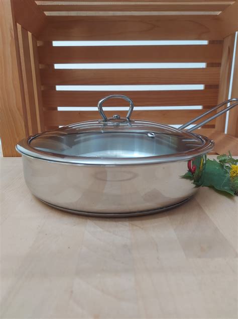 Slika široke, nizke posode iz nerjavečega jekla z debelim dnom, napolnjene z marmelado.