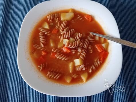 Fotografija krožnika z bogatim piščančjim paprikašem, postreženim s testeninami in žlico kisle smetane.