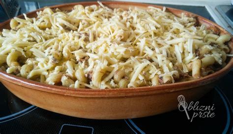 Prikaz postopka priprave gratiniranih testenin, vključno z dodajanjem omake in sira.