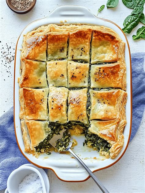 Thematic photo of a spanakopita (Greek spinach pie) cut into pieces on a serving platter.