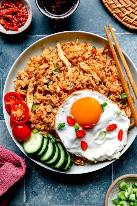 Pripravljen Nasi Goreng na krožniku, okrašen s pečenim jajcem in zelenjavo.