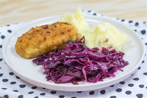 Prikaz sestavin za pripravo dušenega rdečega zelja: rdeče zelje, rdeča čebula, jabolka, vino in začimbe.