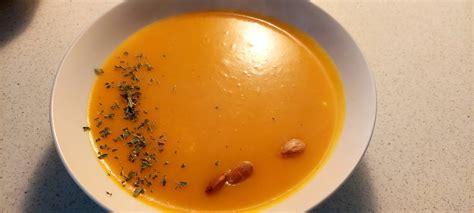 Pripravljena kremna juha iz hokaido buče v skledi, okrašena z bučnimi semeni in kapljico bučnega olja