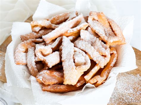 Fotografija lepo oblikovanih pustnih krofov, posutih s sladkorjem v prahu.