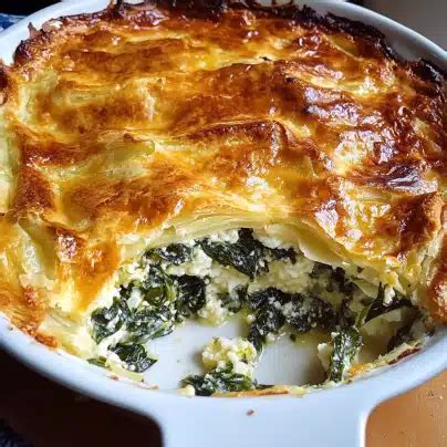 Thematic photo of a spinach and cottage cheese pie on a wooden table, garnished with fresh herbs