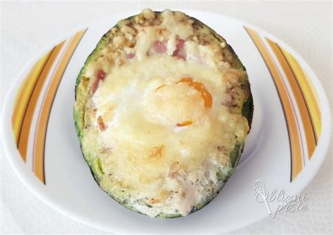 Fotografija pečene polovice avokada z jajcem in koščki dimljenega lososa na vrhu, obdana z zelenjavo.