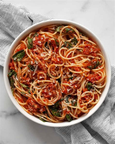A close-up of spaghetti tossed in a vibrant red tomato sauce with fresh basil leaves and a hint of red chili flakes.
