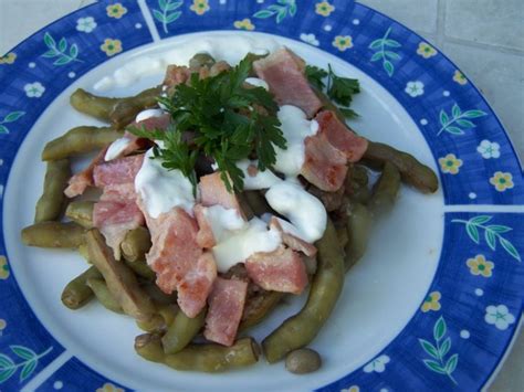 Pripravljen krožnik stročjega fižola s slanino in ocvirki, ki ga prelije smetana.
