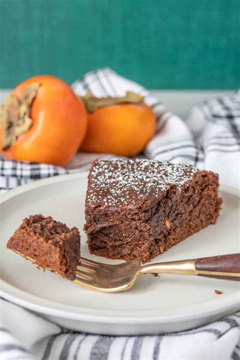 Thematic photo of a slice of chocolate persimmon cake with whole persimmons and autumn leaves