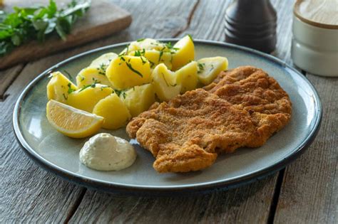 Serviran dunajski zrezek z rezino limone, peteršiljevim krompirjem in solato.