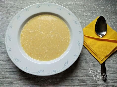 Fotografija servirane kremne cvetačne juhe v globokem krožniku s kapljico kisle smetane in svežimi zelišči.