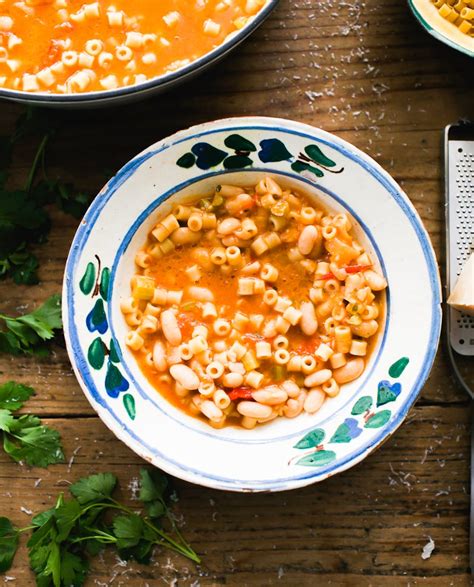 The final dish of pasta e fagioli in a bowl, garnished with fresh parsley and a drizzle of olive oil, with a slice of bread on the side.