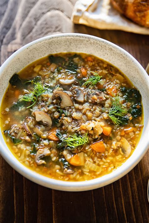 Thematic photo of a steaming bowl of traditional mushroom soup with buckwheat groats and diced potatoes, garnished with fresh parsley and a dollop of sour cream, on a wooden table.
