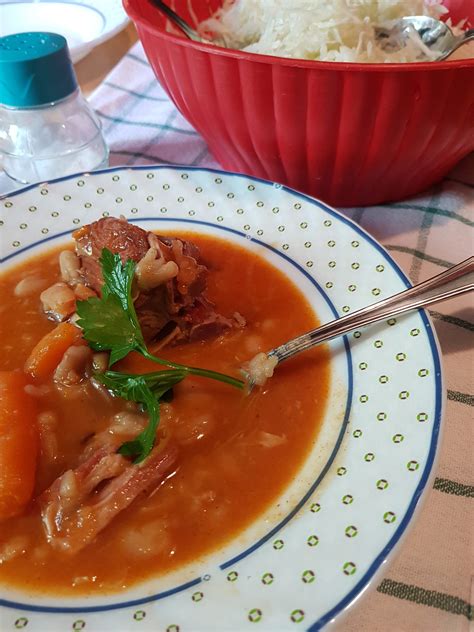 Fotografija tradicionalnega srbskega pasulja s kosom dimljenega mesa, postreženega v glineni skledi