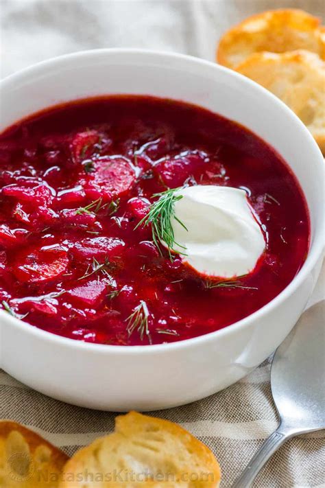 Thematic photo of a bowl of red beet soup (borscht) garnished with sour cream and herbs.