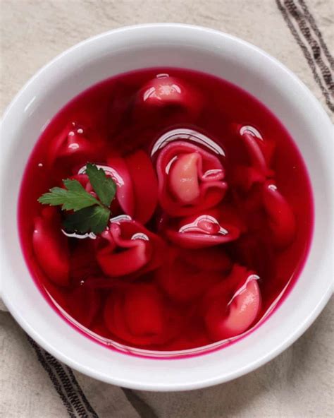 Photo of a serving of clear red borscht (barszcz czerwony) in a traditional cup with two handles, accompanied by small pastries.