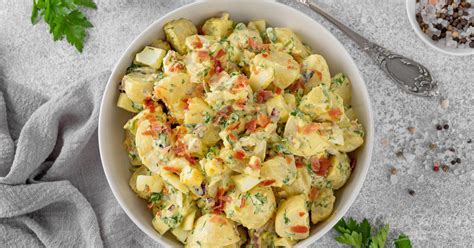 Prikaz pripravljene klasične krompirjeve solate z delikatesnimi kumaricami, jajci in zelišči.