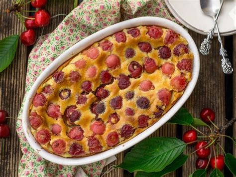 Prikaz pečenega, zlato rjavega skutnega zvitka s češnjami, posutega s sladkorjem v prahu.