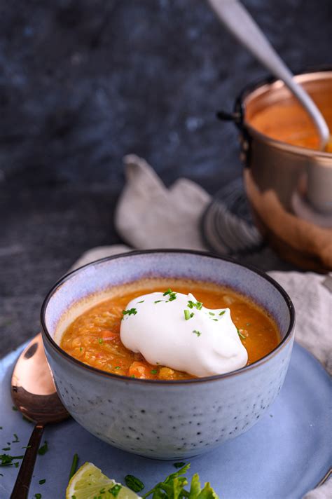 kuhana juha iz rdeče leče v skodelici, okrašena s peteršiljem in kapljico limoninega soka