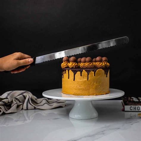 The image should show a person using a long serrated knife to cut a cake sponge on a rotating cake stand.