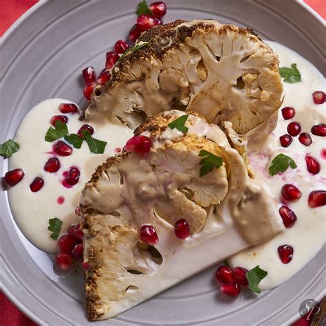 Tematična fotografija: Cela pečena cvetača s tahini in jogurtovo omako, posuta z granatnim jabolkom in zelišči.