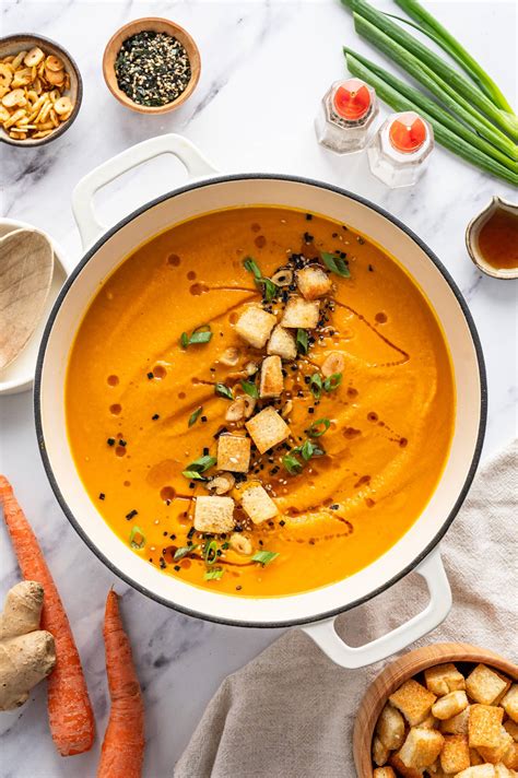 Thematic photo of a cozy, steaming bowl of carrot ginger soup garnished with croutons and herbs, with festive background elements.