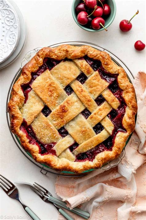 A slice of cherry and mascarpone pie on a plate, with fresh cherries and a glass of elderflower juice