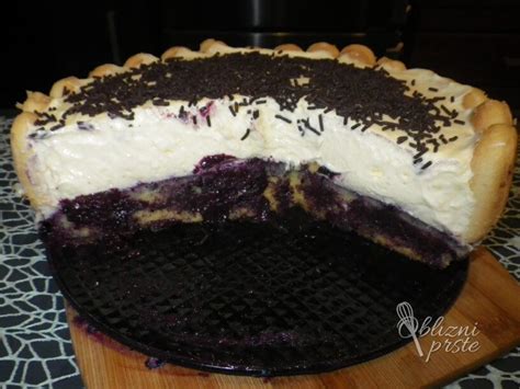 Fotografija dobro ohlajene borovničeve torte, okrašene s čokoladnimi ostružki, svežimi borovnicami in lističi mete